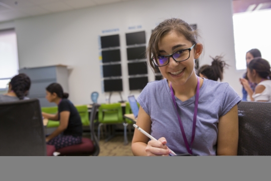 Image of a K-12 student smiling at the camera while using a tablet